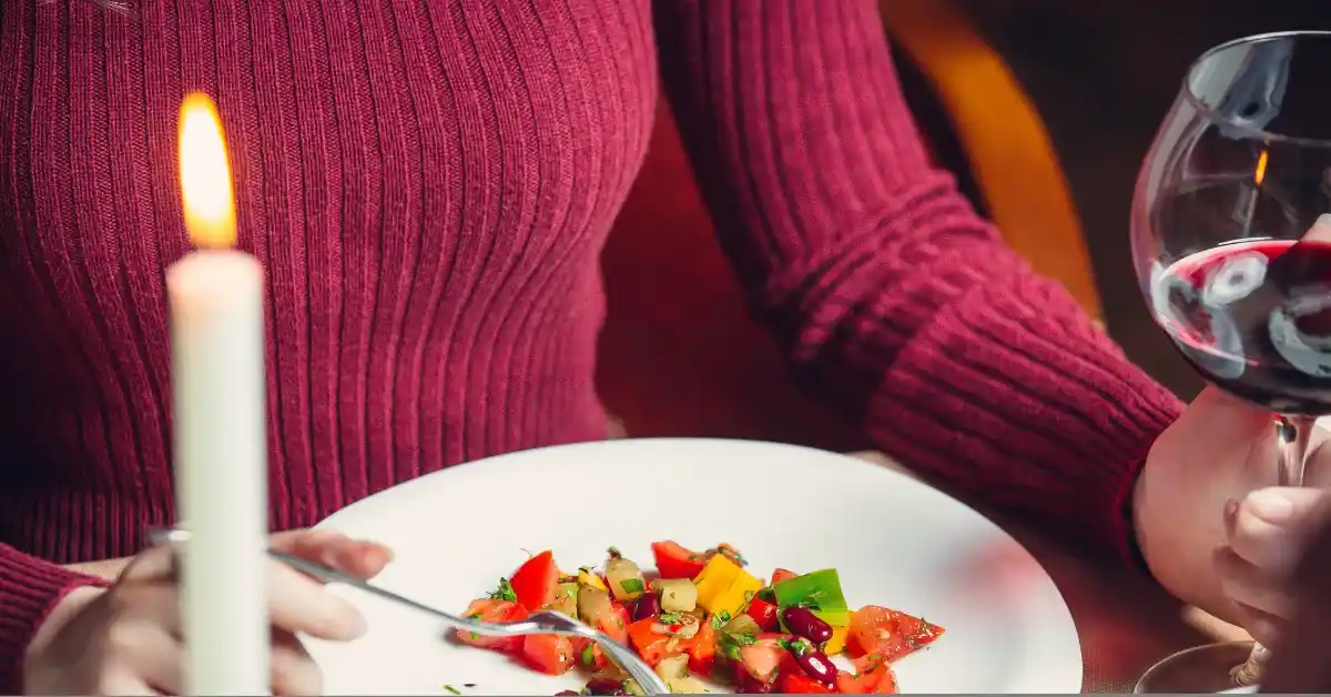 Woman enjoying a candlelight dinner with a fresh vegetable salad and a glass of red wine at a romantic table setting.