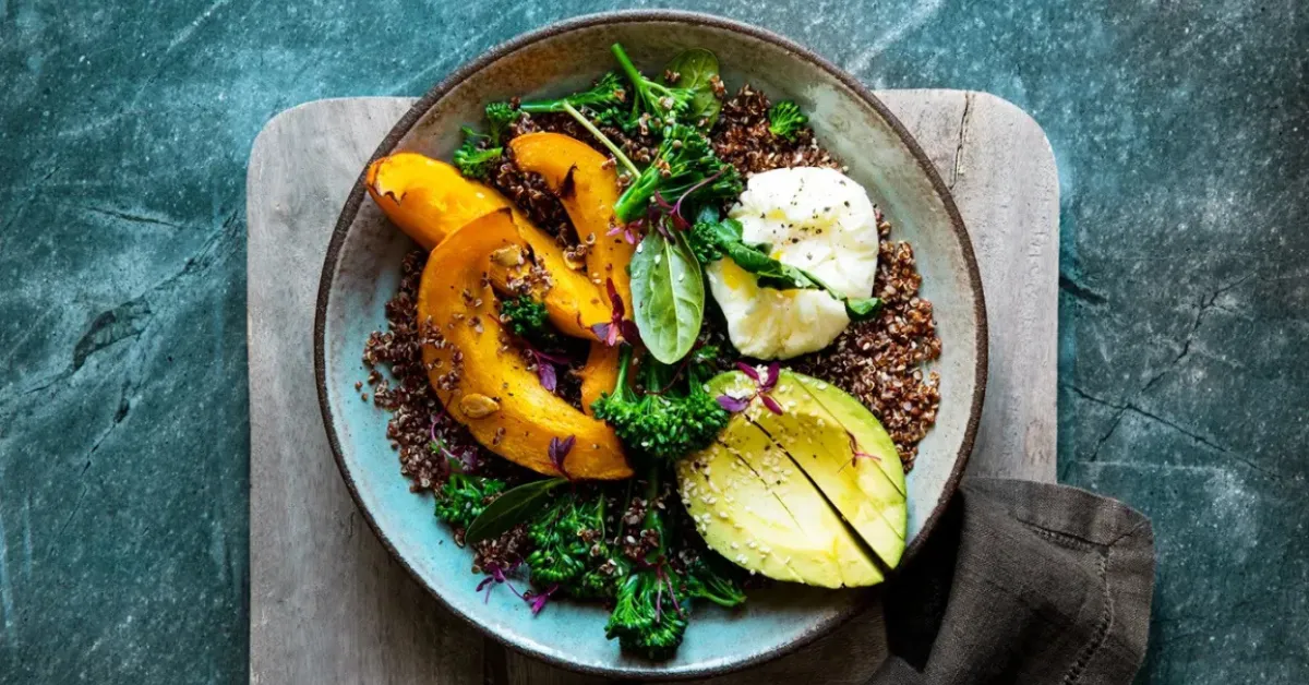 Healthy quinoa bowl with roasted pumpkin slices, avocado, poached egg, and fresh greens on a rustic plate.